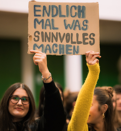 Zwei Schülerinnen halten ein Plakat hoch: Endlich mal was Sinnvolles machen