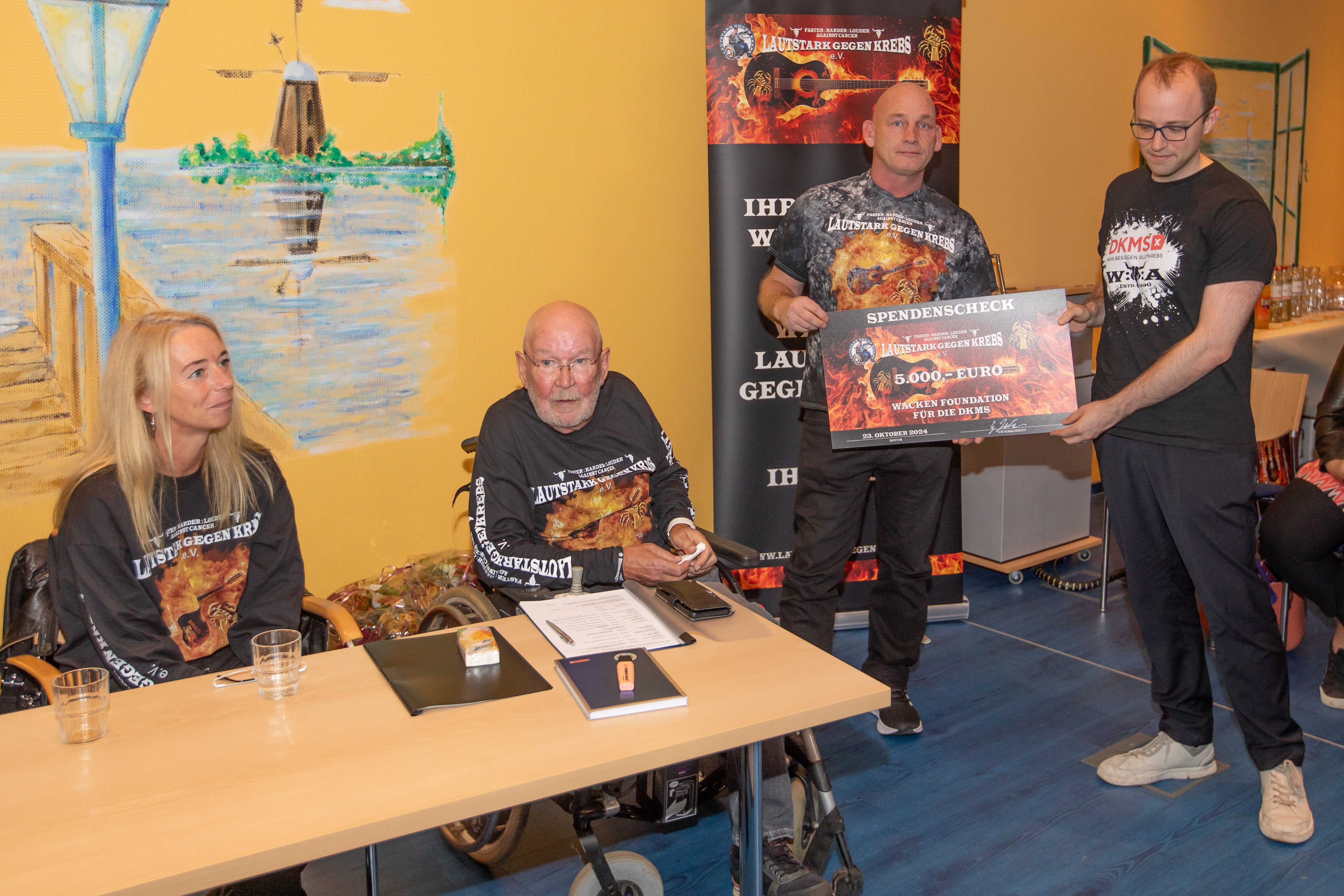 "Wackenopa" Günter Jacobs überreicht DKMS Volunteer Felix den symbolischen Scheck