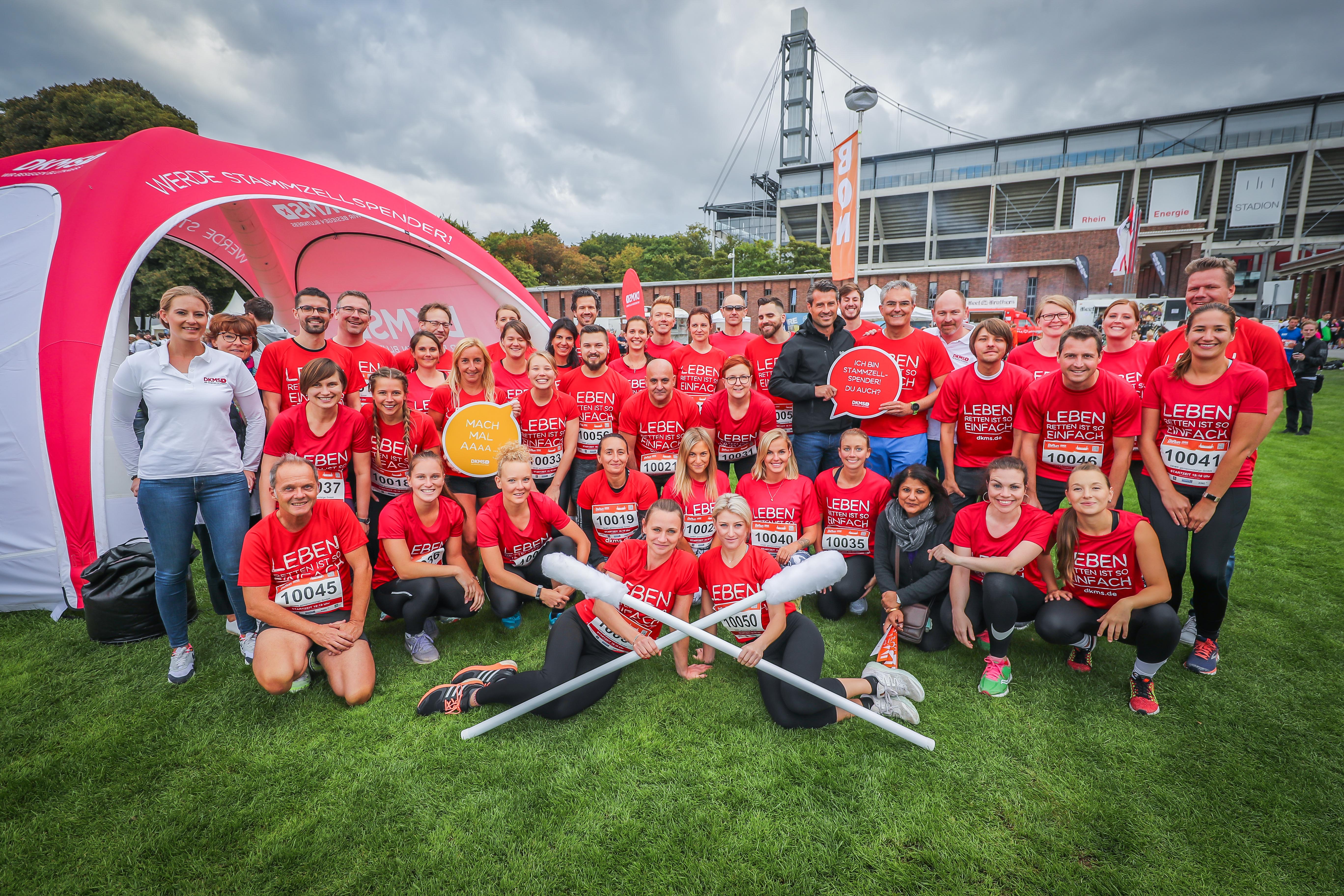 Gruppenfoto von DKMS-Mitarbeitenden in roten „Leben Spenden Läuft“-Shirts vor einem Zelt auf einer Wiese.
