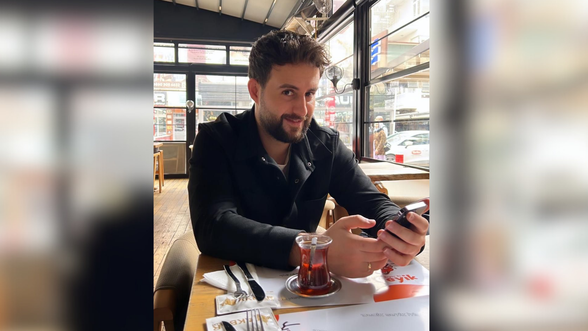 Ein Mann sitzt an einem Tisch und hält ein Smartphone in den Händen.