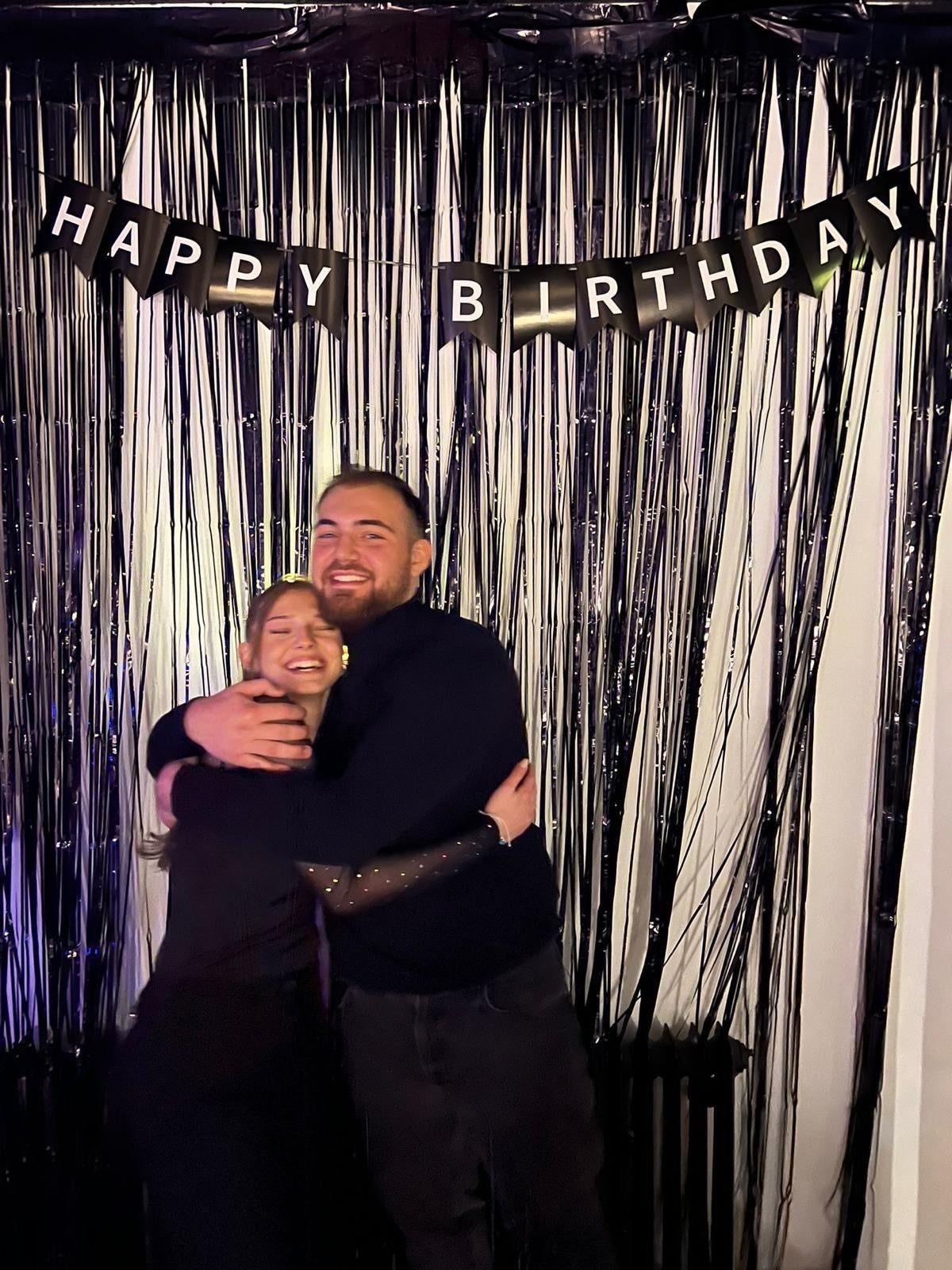 Ein Mann und eine Frau umarmen sich vor einem Geburtstagsbanner