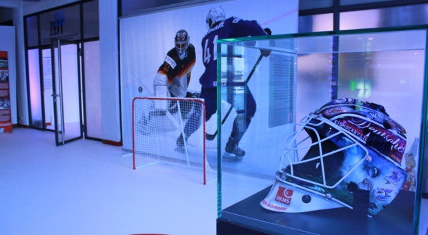 Hockeyhelm in einer Vitrine auf einem Hockeyfeld mit Tor