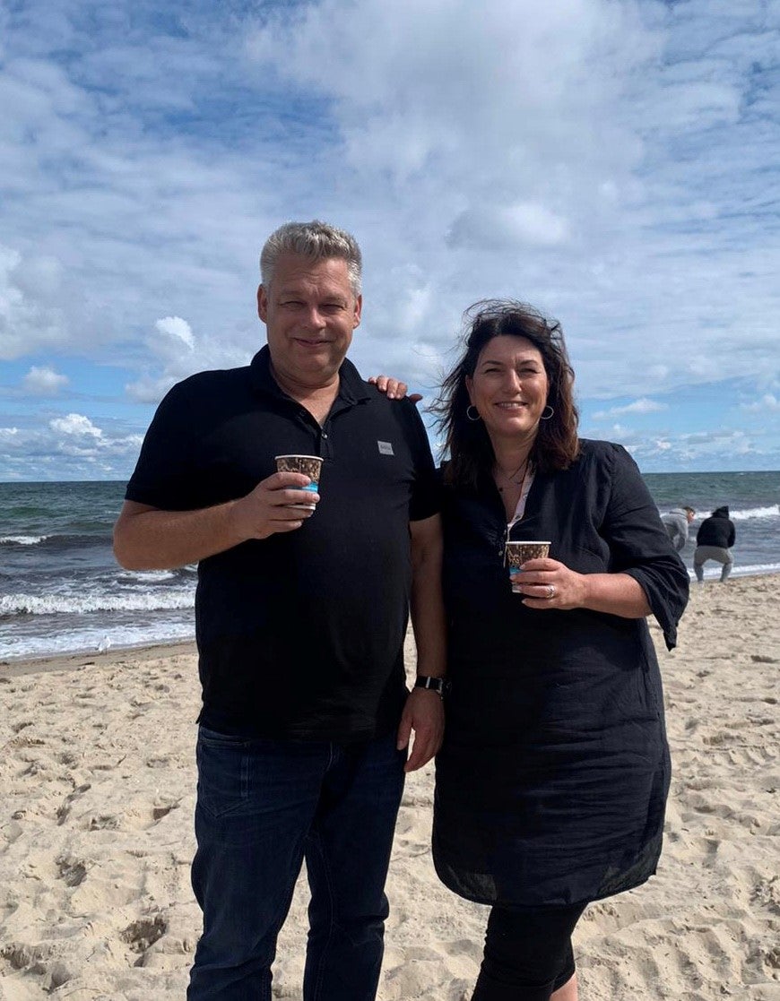 Ein Mann und eine Frau stehen an einem Strand und halten Tassen mit Kaffee