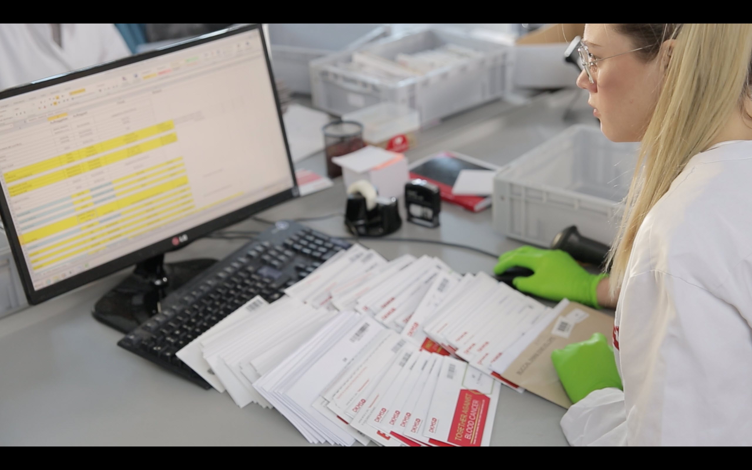 Eine Frau im Laborkittel und mit Handschuhen schaut auf einen Computerbildschirm