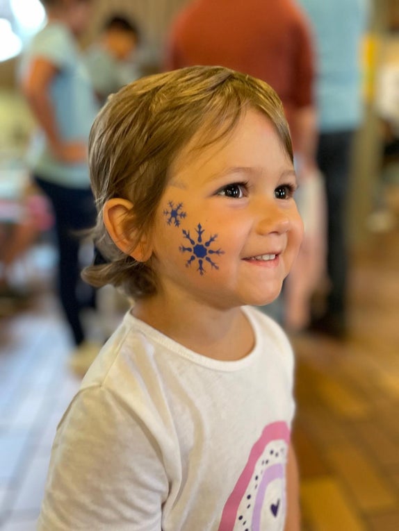 Malina lächelt in die Kamera. Auf ihrer rechten Gesichtshälfte hat sie ein Tattoo. 