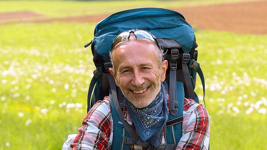 Fuat Gören mit einem Rucksack. Im Hintergrund ist eine Blumenwiese.