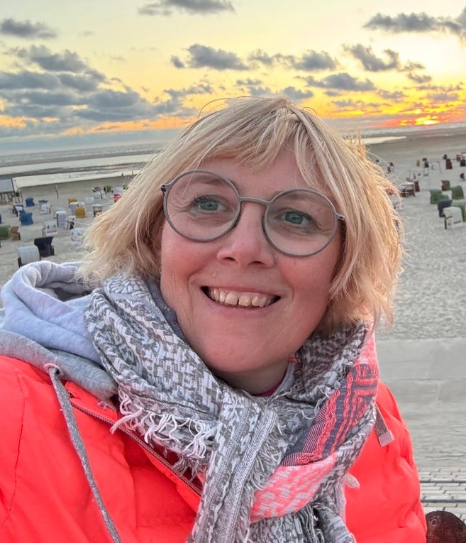 Eine Frau lächelt am Strand in die Kamera