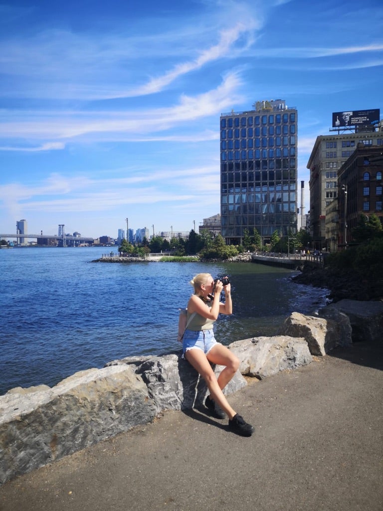 Stella in den USA, sie steht vor einem Gewässer und hält eine Kamera 