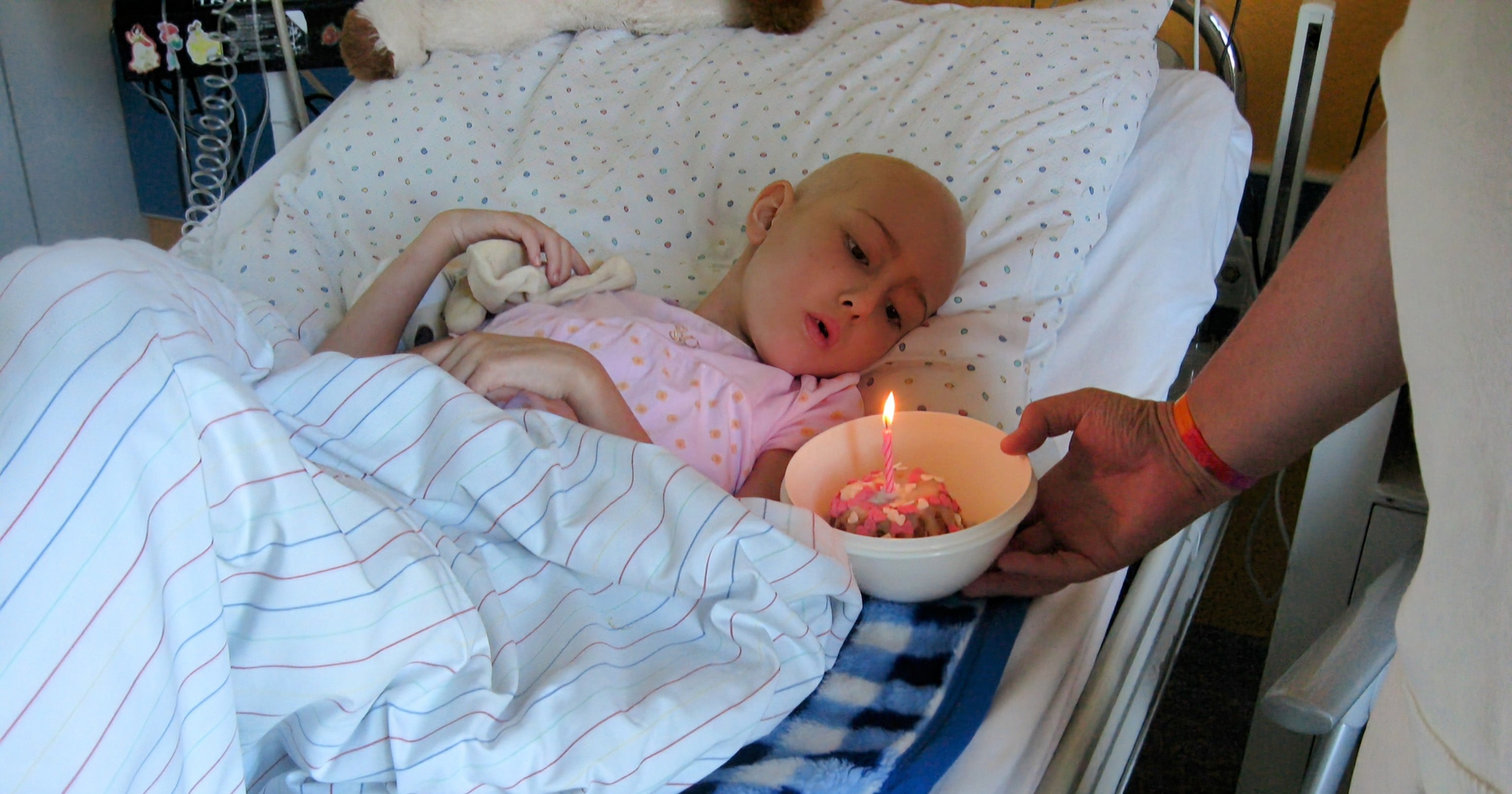 Ein Kind liegt in einem Krankenhausbett und bekommt ein Stück Kuchen mit einer Kerze hingehalten