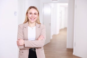 Eine Frau lächelt mit verschränkten Armen in einem Hausflur