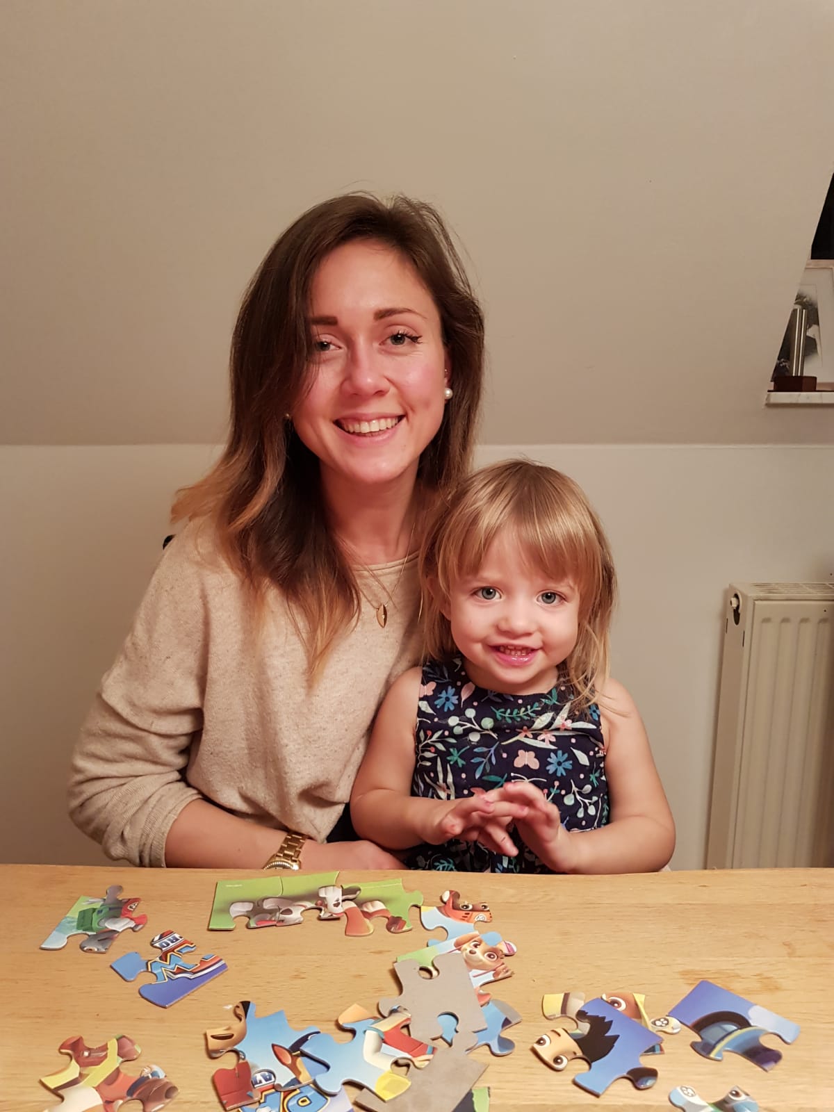 Anika und Hannah lächeln für die Kamera, sie puzzeln zusammen an einem Tisch
