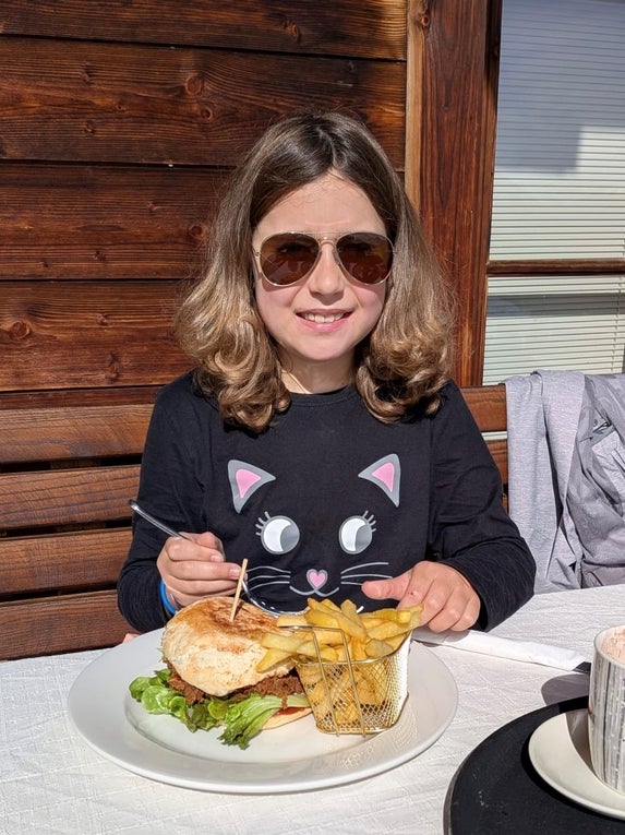Ein Mädchen mit Sonnenbrille während sie einen Burger mit Pommes isst.