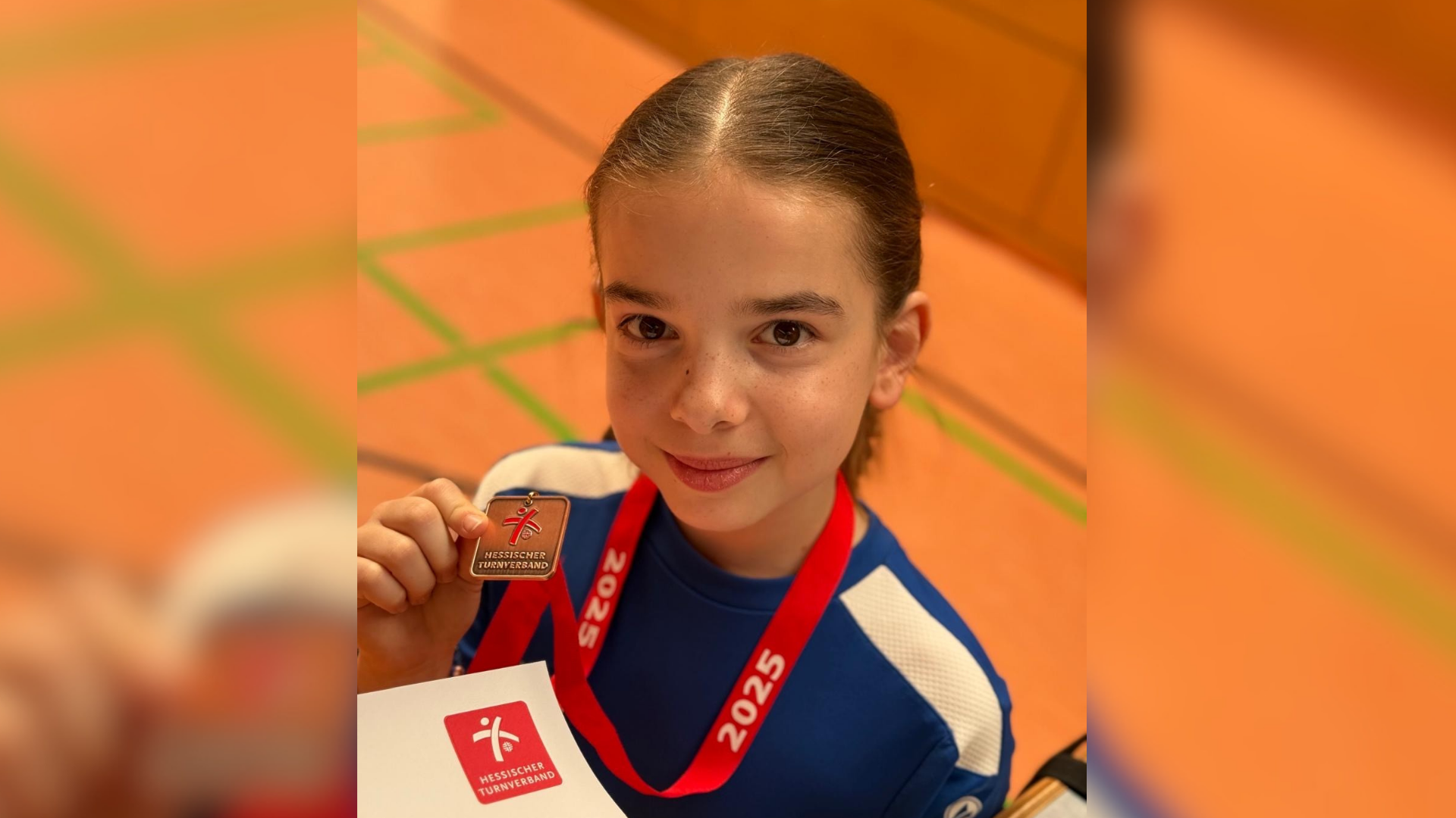 Ein Mädchen hält eine Medaille in die Kamera. 