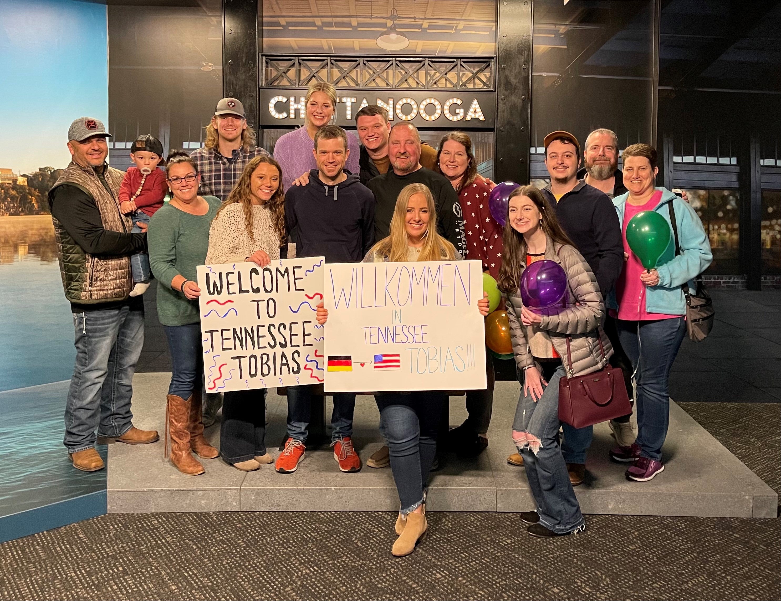 Eine Gruppe von Menschen posiert für ein Foto, sie halten Wilkommens-Schilder hoch