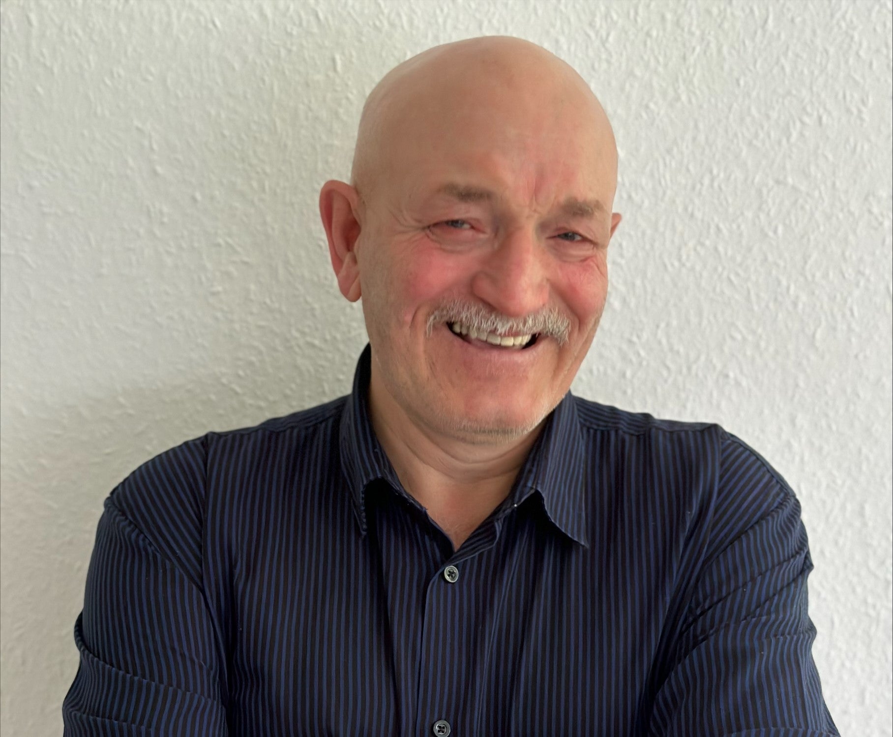 Mann mit Glatze und Schnäuzer lächelt in die Kamera