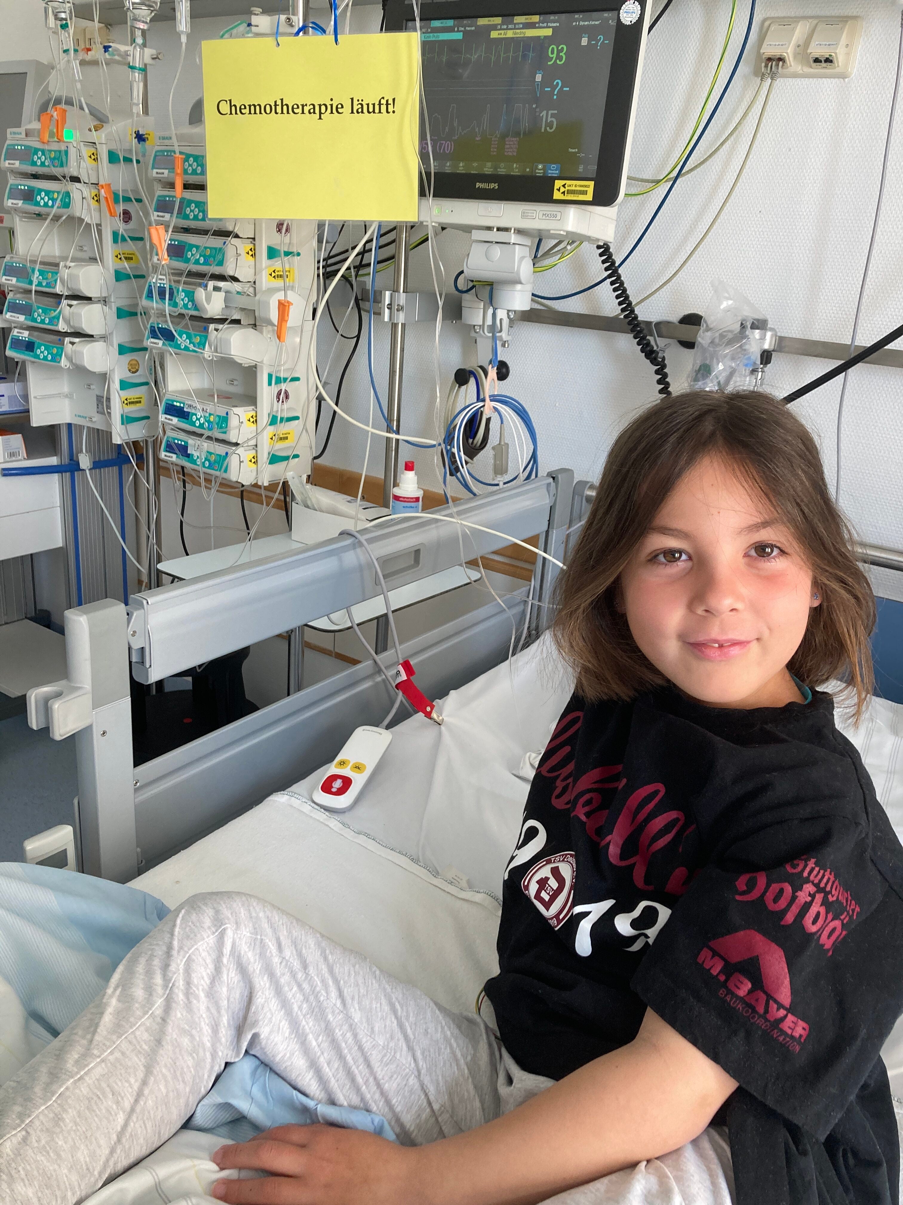 Hannah sitzt auf einem Bett während eine Chemotherapie läuft