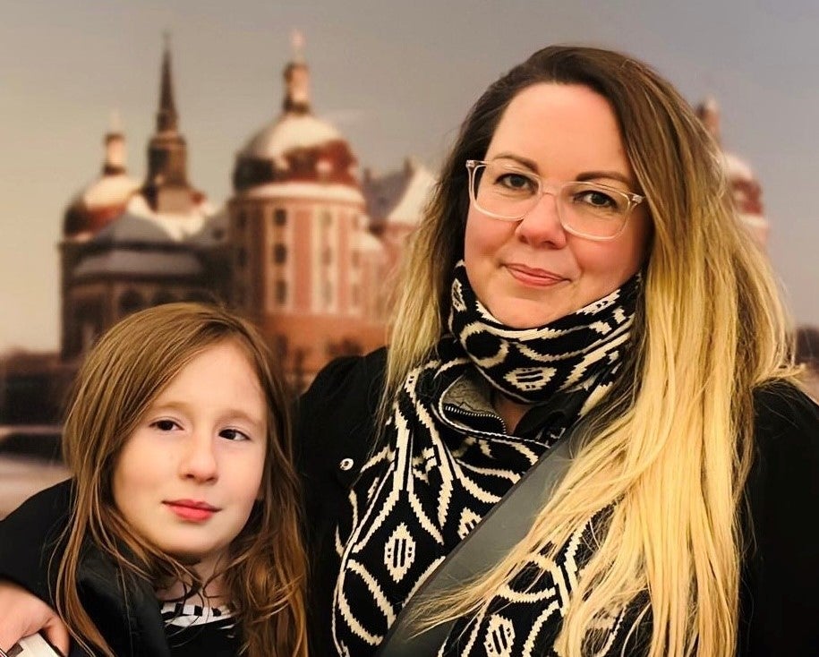 Eine Frau mit Brille und Schal legt ihren Arm um ein Mädchen.