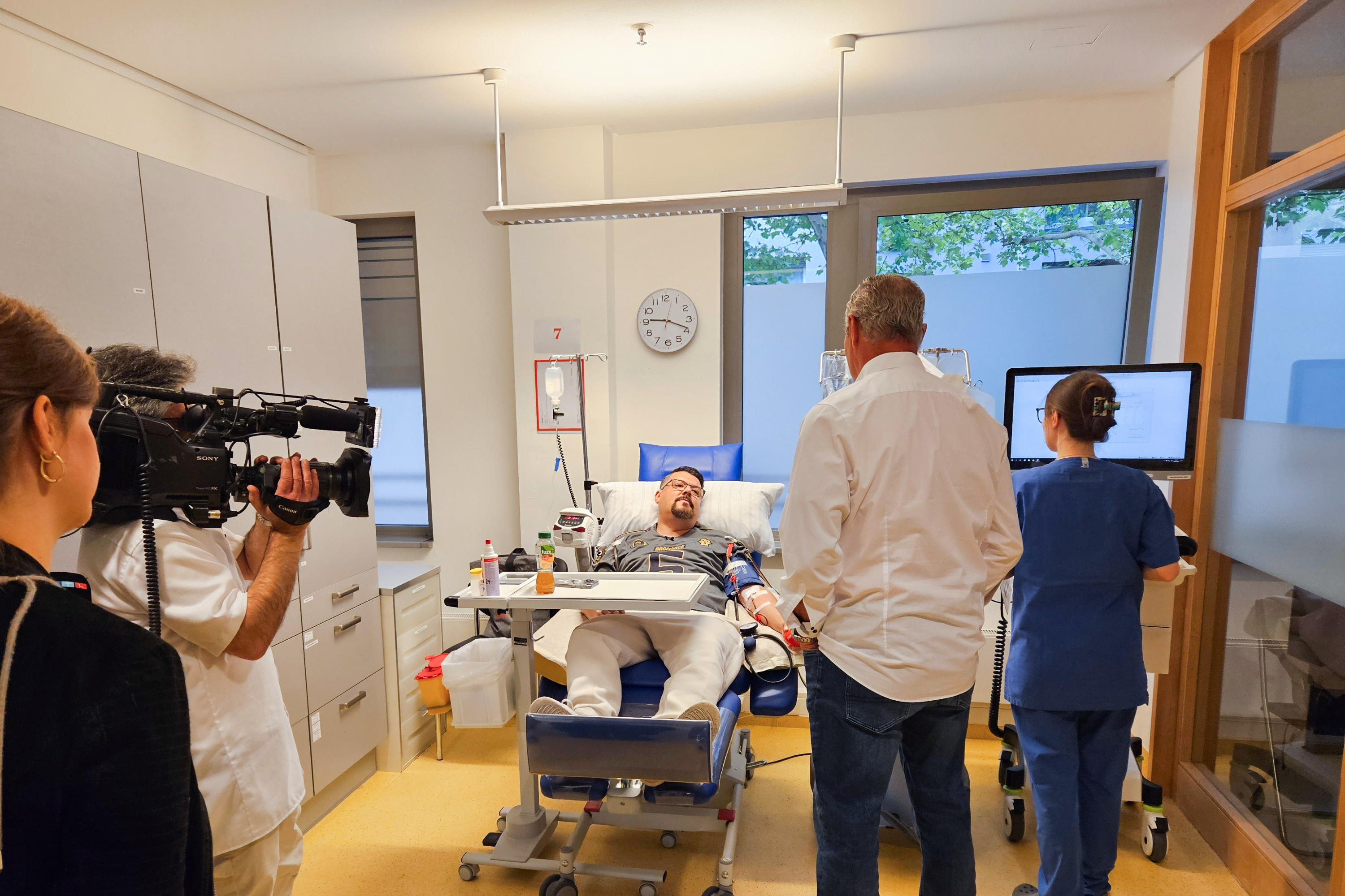 Ein Mann liegt in einem Krankenhausbett mit einem Mann auf einem Stuhl.