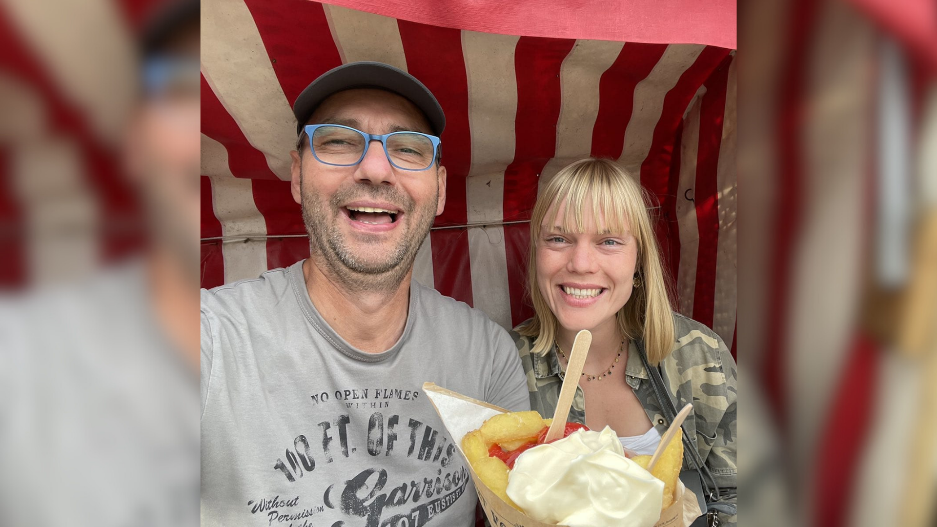 Ein Mann und eine Frau sitzen lachend in einem rot-weiß gestreiften Strandkorb mit einer Tüte Pommes Frites.