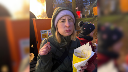 Eine Frau isst aus einer Tüte Pommes und kneift dabei die Augen zu. 