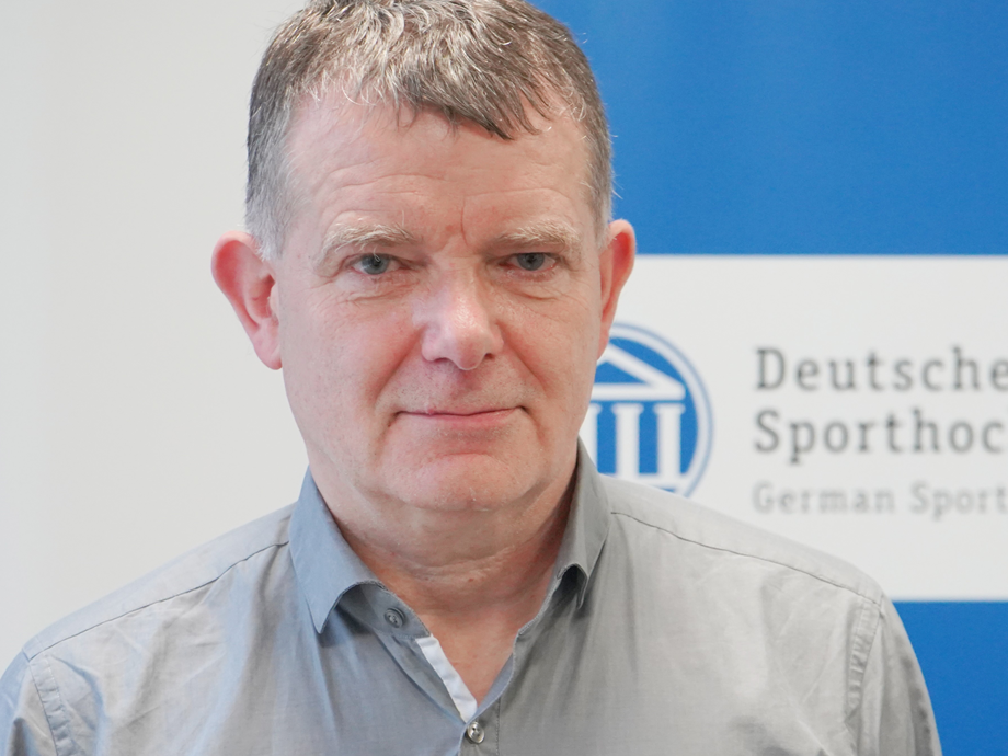 Ein Mann in einem grauen Hemd, im Hintergrund das Spoho Logo Köln