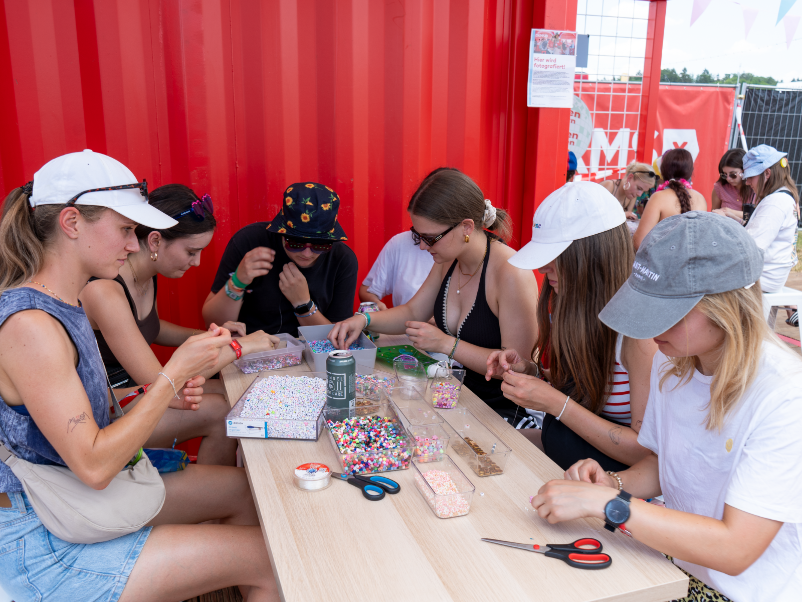 Eine Gruppe junger Leute bastelt am Stand der DKMS auf dem Southside Festival Armbänder