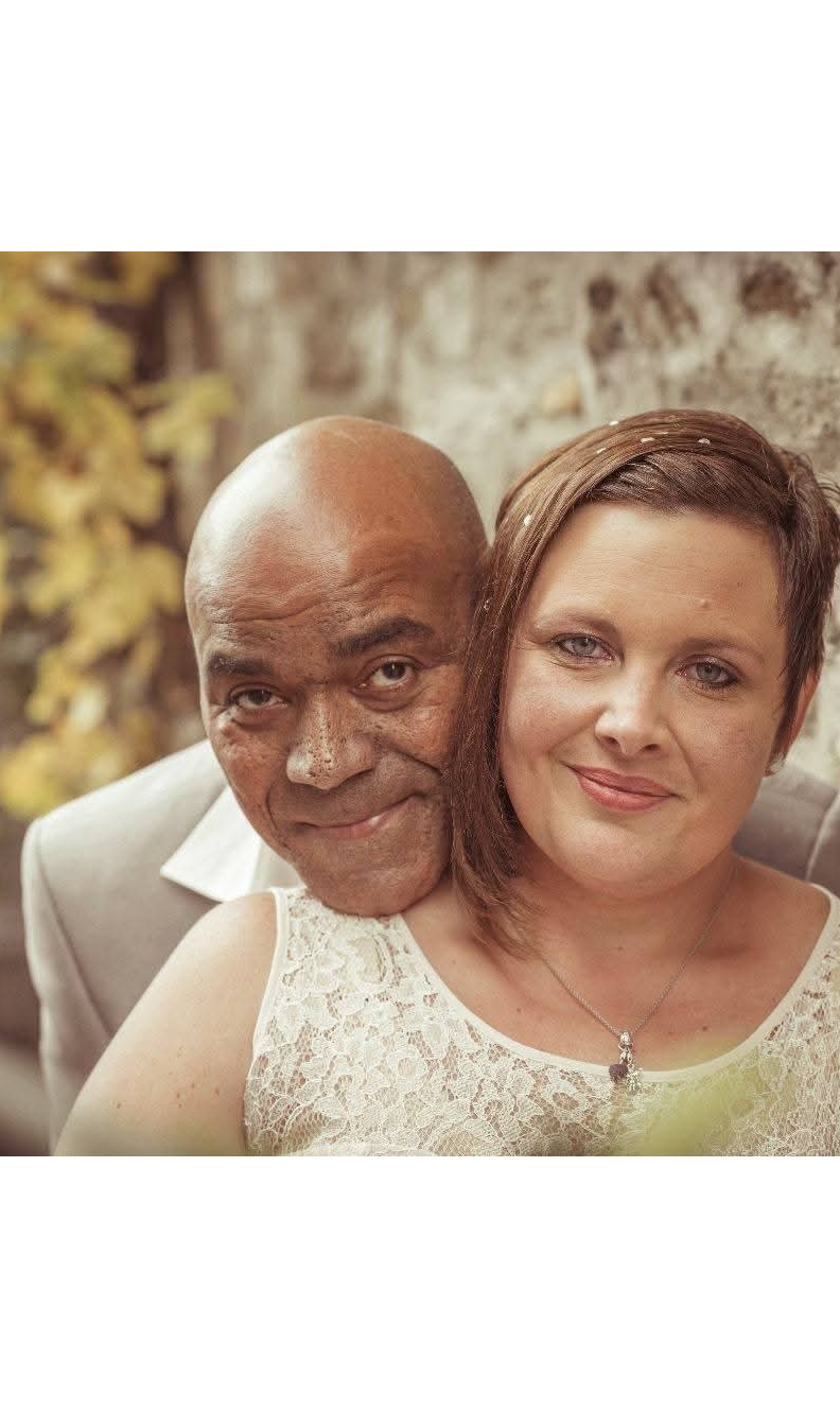 Ein verheiratetes Paar posiert für ein Hochzeitsfoto. Die Frau steht im Vordergrund, der Mann steht dahinter und umarmt die Frau