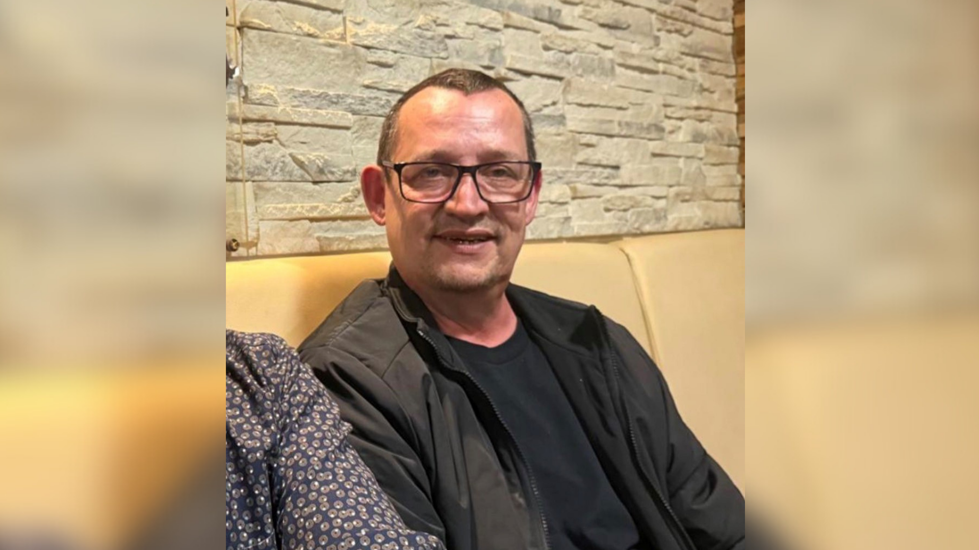 Ein Mann trägt Brille und sitzt auf einer gelben Ledercouch. 