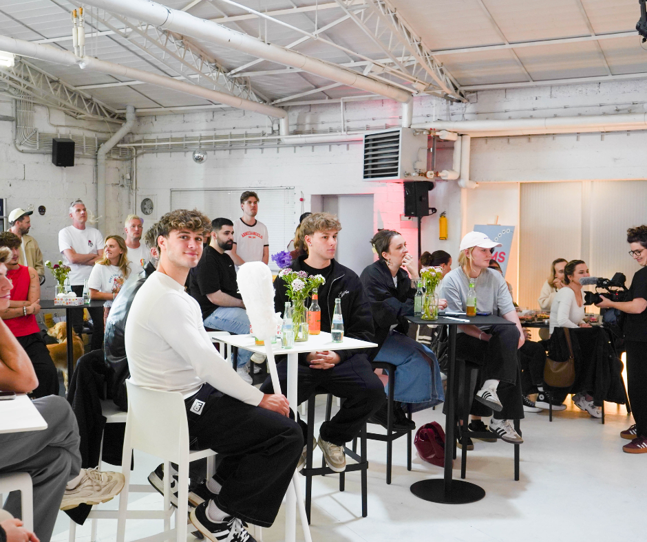 Eine Gruppe von Menschen sitzt an Tischen in einem Raum mit einer großen weißen Wand