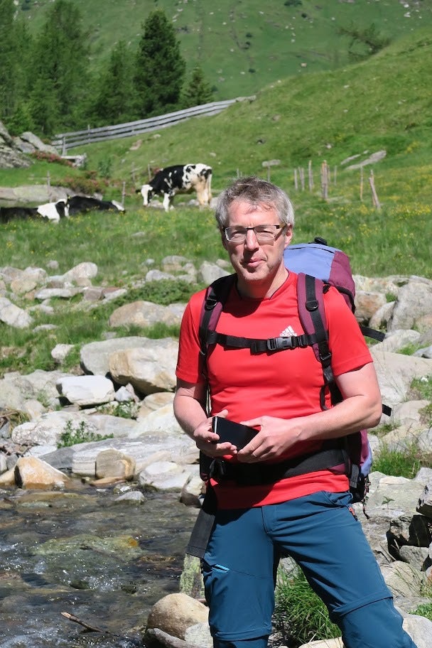 Ein Mann steht vor einem Fluss mit einer Kuh im Hintergrund