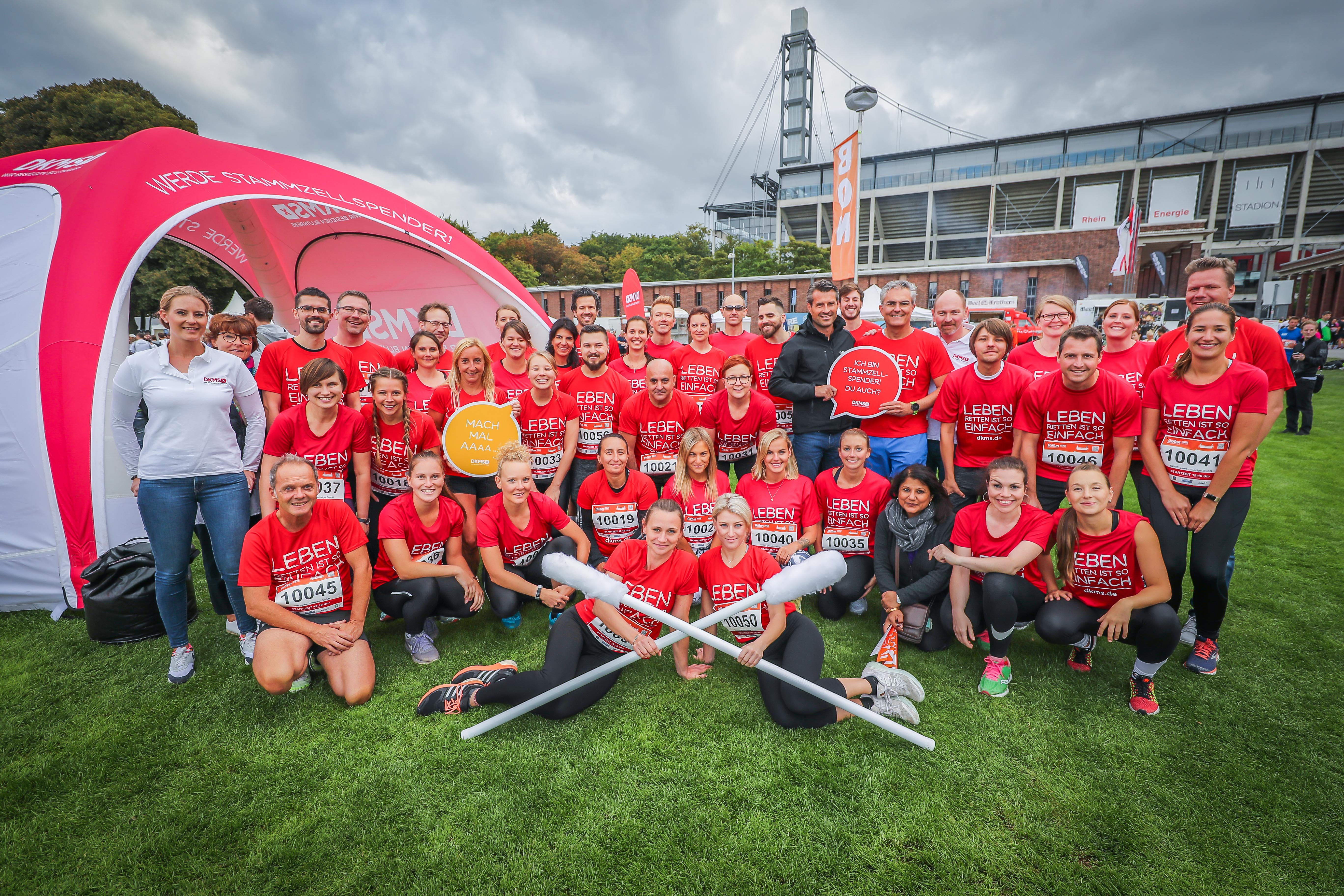 Gruppenfoto von DKMS-Mitarbeitenden in roten „Leben Spenden Läuft“-Shirts vor einem Zelt auf einer Wiese.