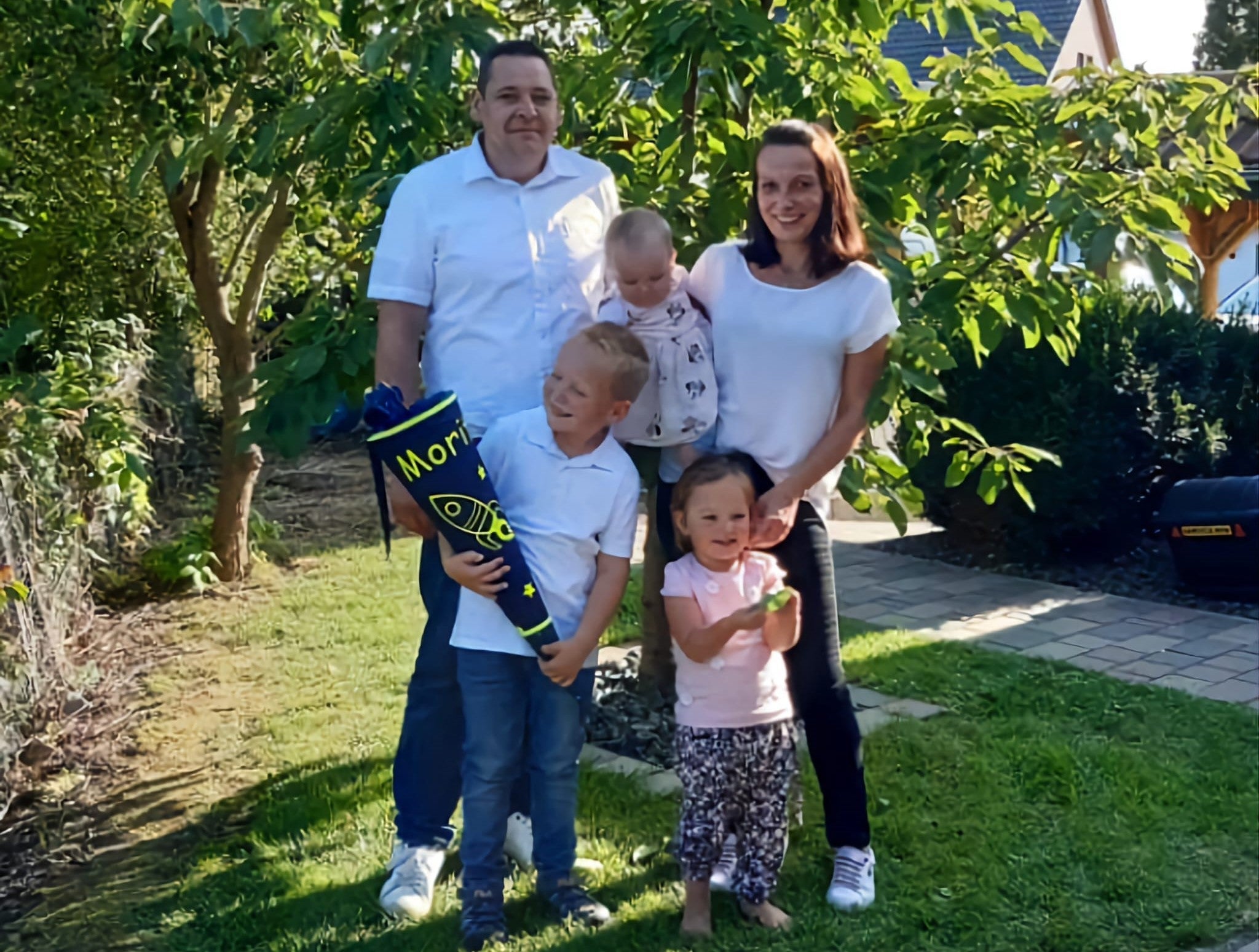 Eine Familie steht im Garten, eines der Kinder hält eine Einschulungstüte.