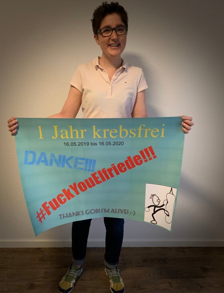 Vanessa hält ein Schild mit der Aufschrift "1 Jahr krebsfrei"