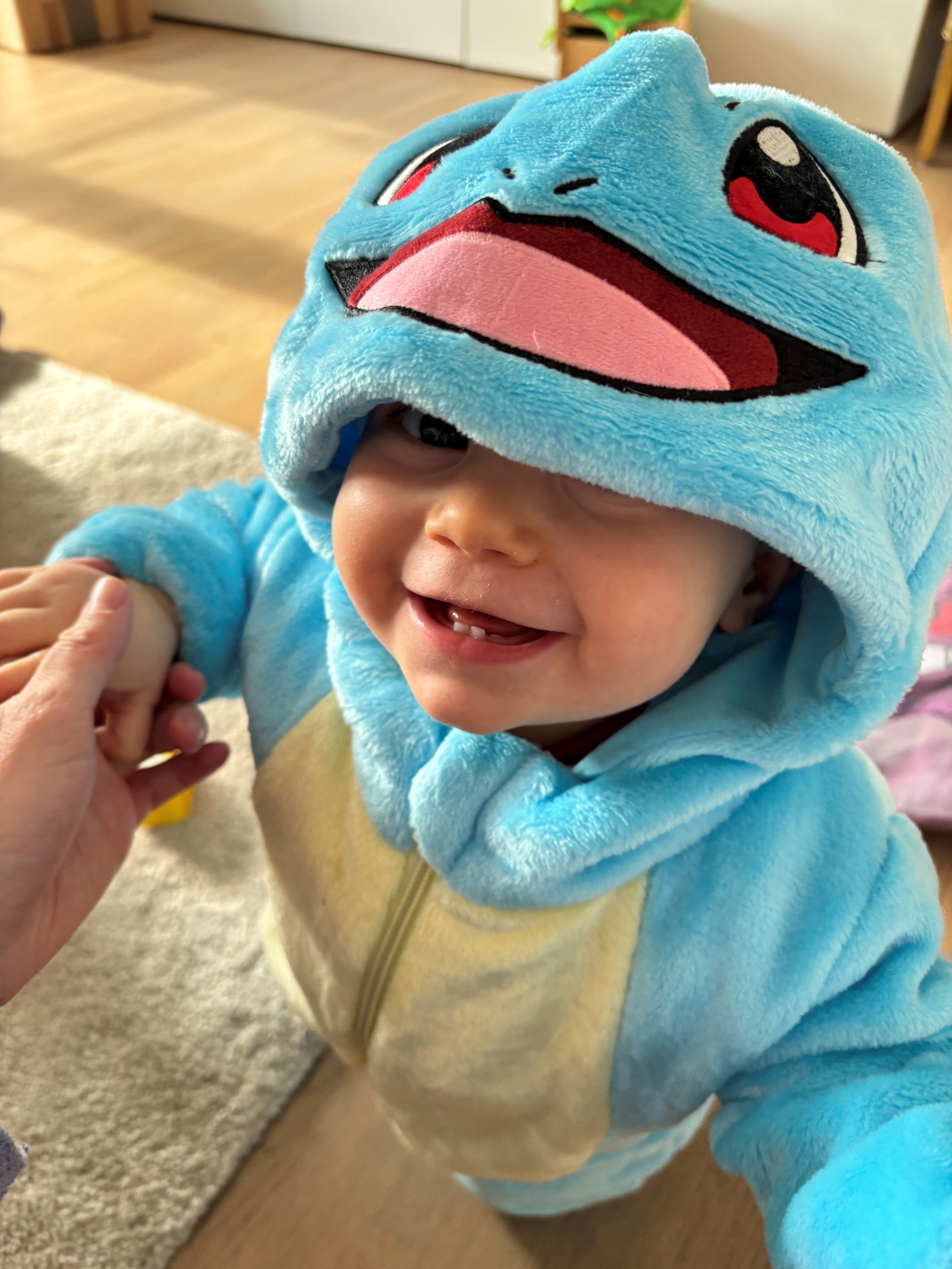 Ein Kleinkind in einem süßen, hellblauen Kostüm, das wie ein Cartoon-Wassertier aussieht.