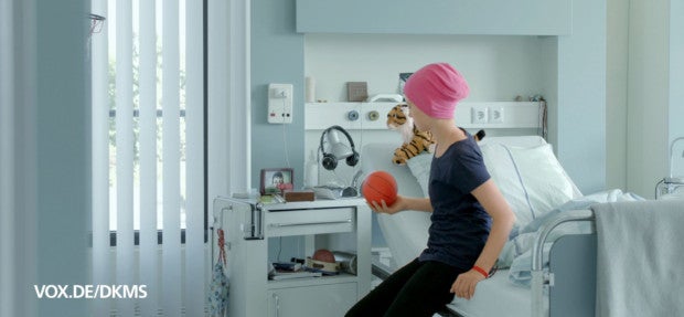 Screenshot aus einem Werbespot. Rinah sitzt auf einem Bett eines Krankenhauszimmers. Links unten im Bild der Text vox.de/dkms
