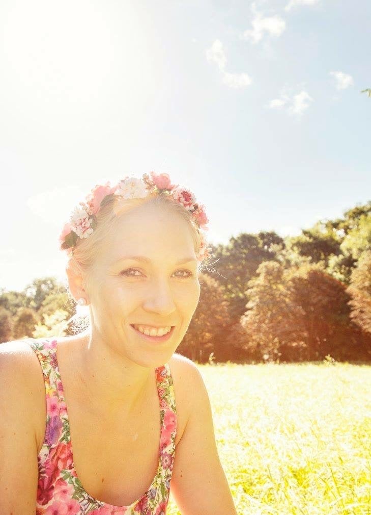 Stella trägt einen Blumenkranz auf dem Kopf und sitzt auf einer Wiese