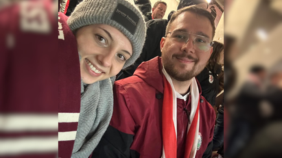 Eine Frau und ein Mann tragen Fanartikel eines Sportvereins und nehmen ein Selfie auf. 