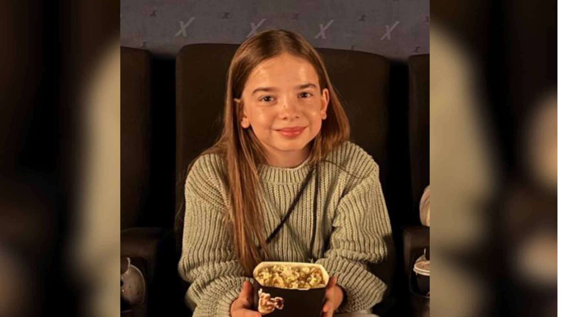 Ein Mädchen sitzt in einem Kinosessel und hält eine Tüte Popcorn in den Händen.