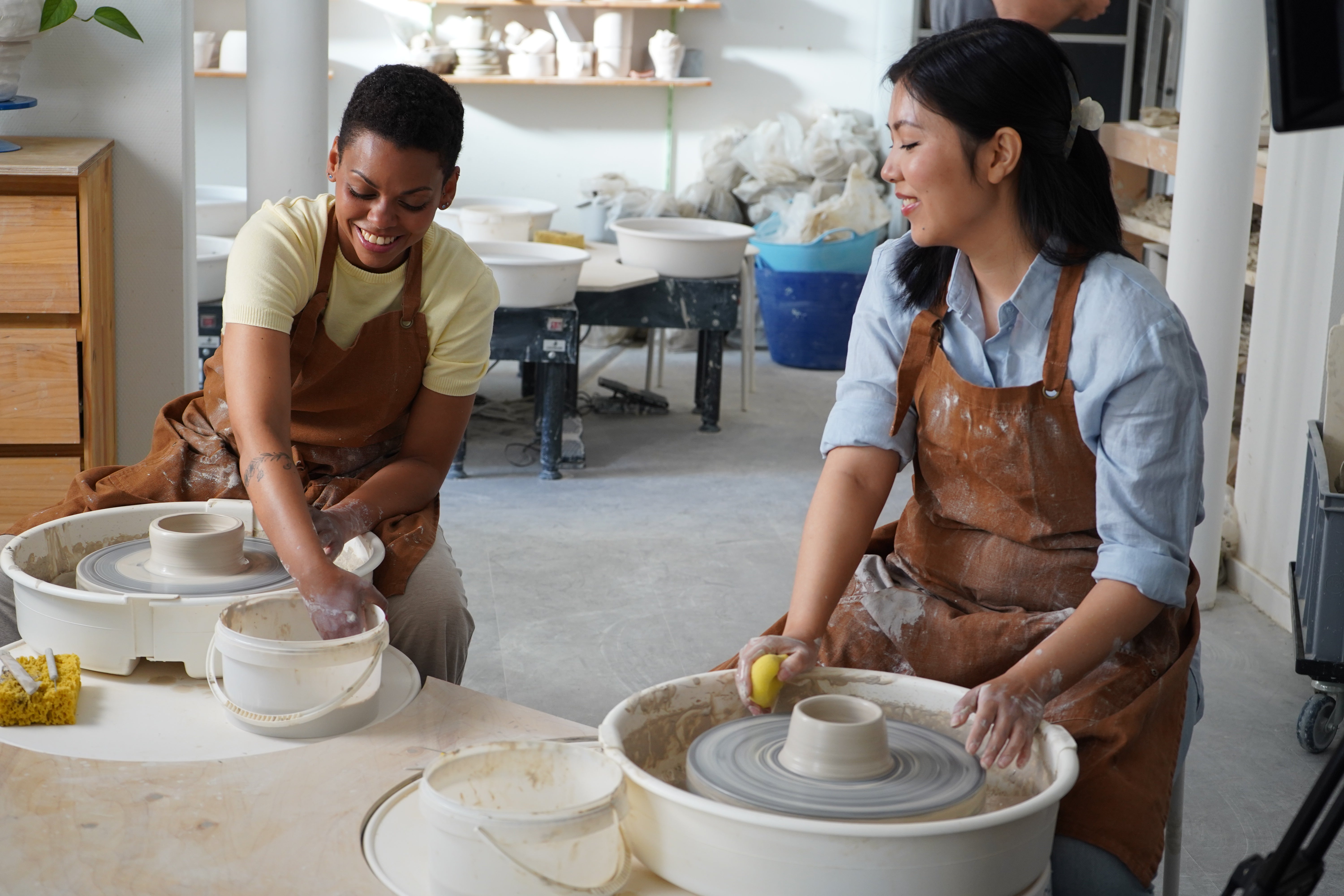 Zwei Frauen sitzen an Töpferscheiben und arbeiten mit Ton.