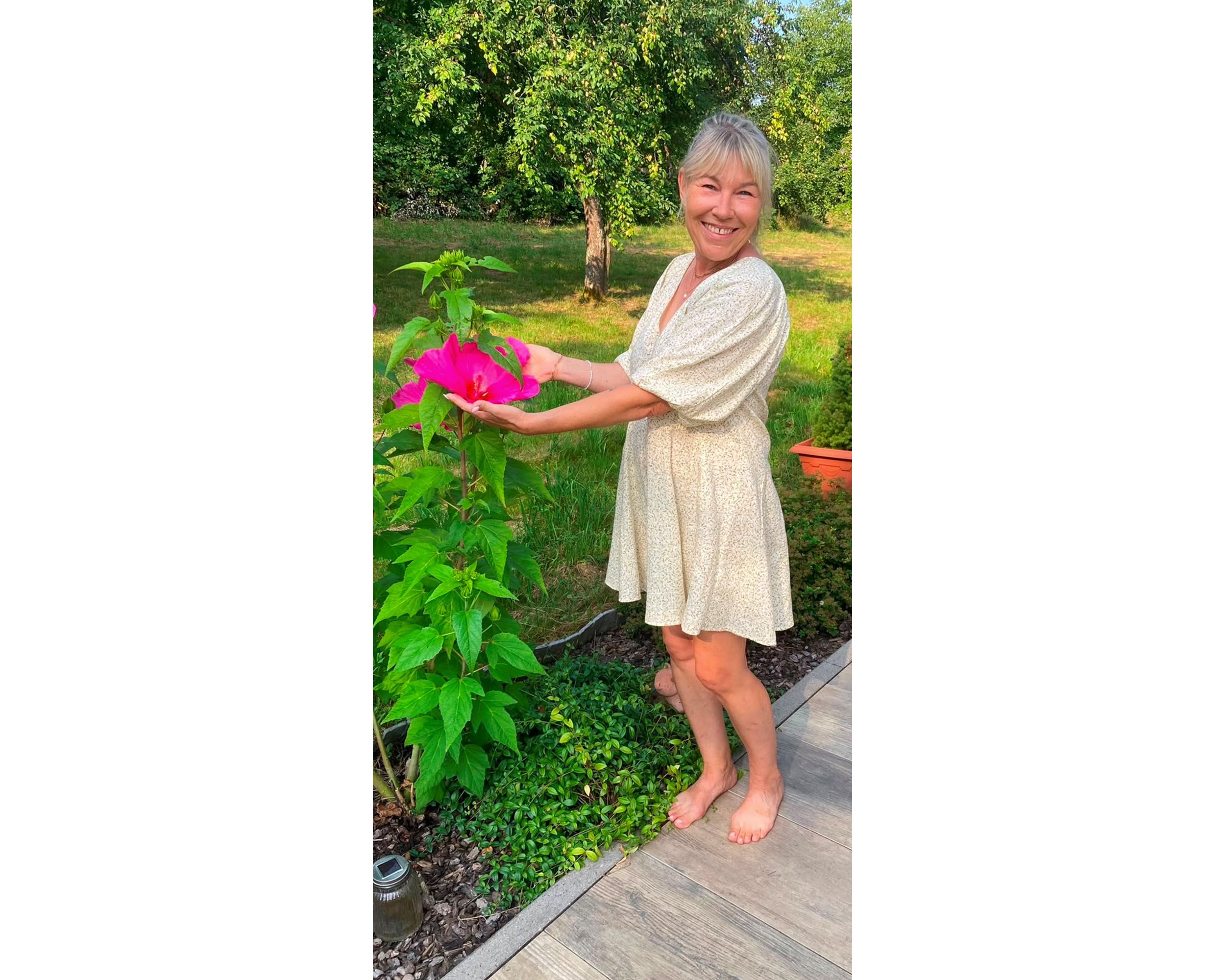 Patientin Britta in einem Garten neben einer pinken Blume. 
