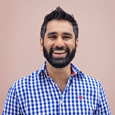 A photo of Dr Amit patel smiling. He has short, dark hair and a beard and is wearing a blue and white checked shirt.