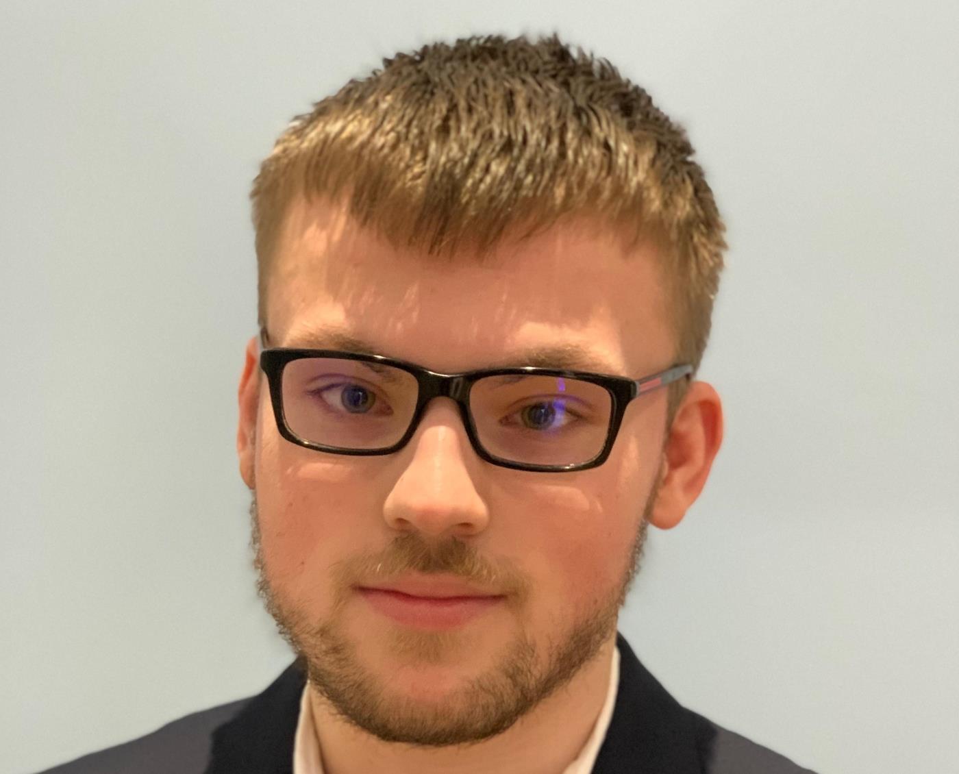 Young man in a black jacket with brown hair and glasses