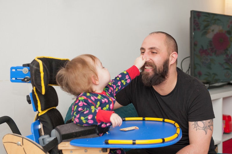 An 18 month old girl pinches her dad's nose. They both laugh.