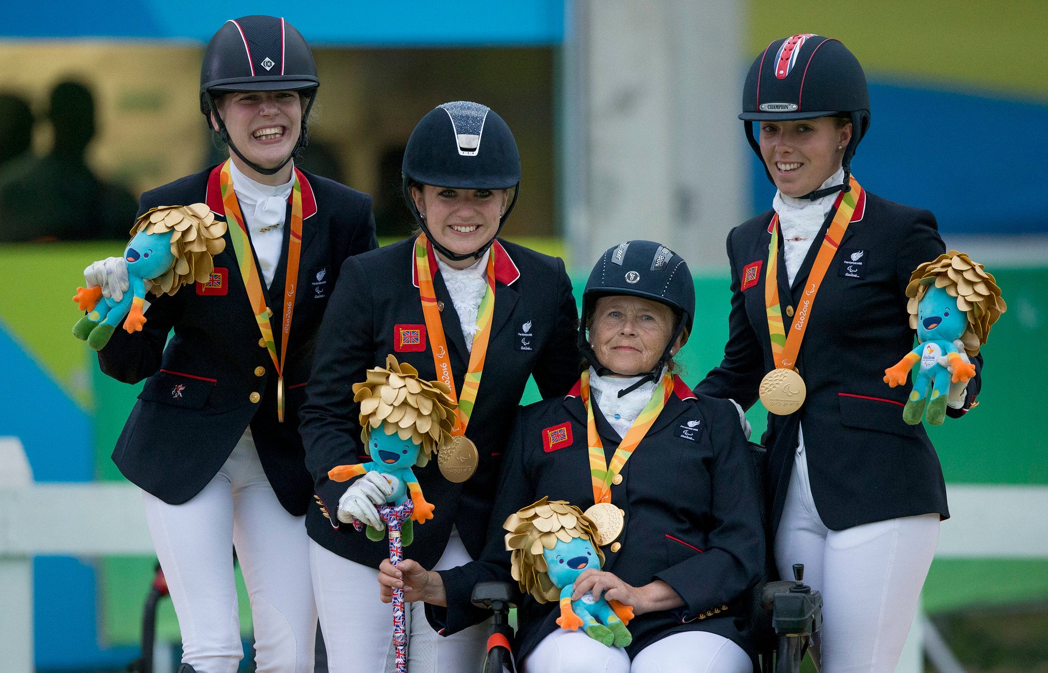 Four people in equestrian outfits holding the Rio 2016 mascot and wearing gold medals