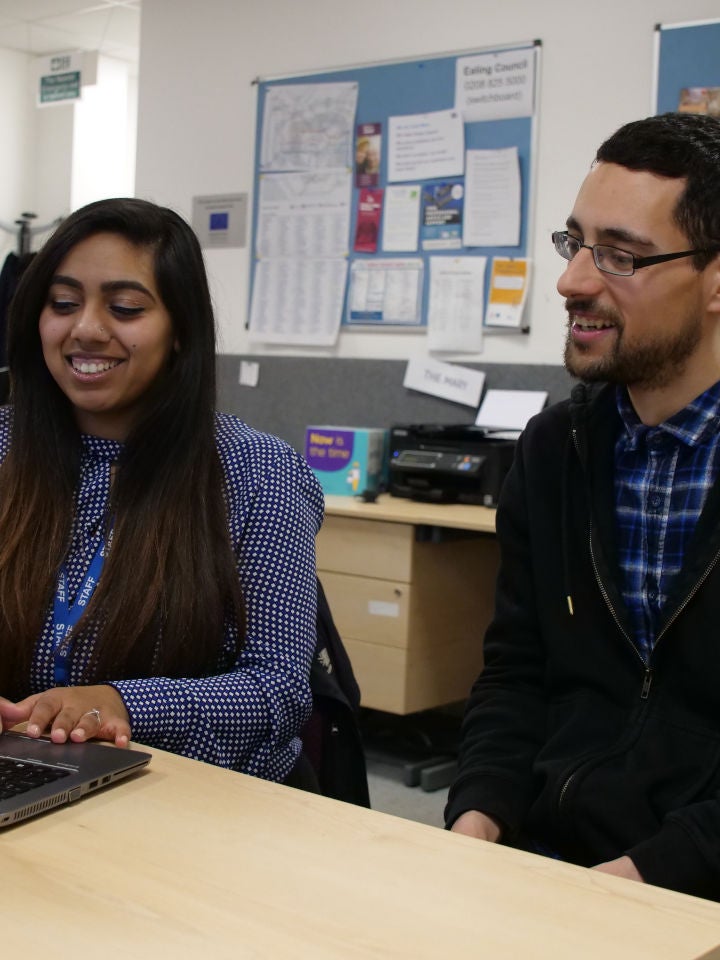 A laughing and smiling young woman and man sat at a desk with laptop in an office