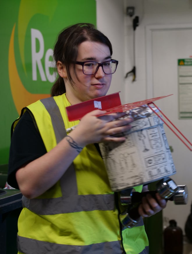 A young woman in a high visibility jacket stocking shelves in a charity shop