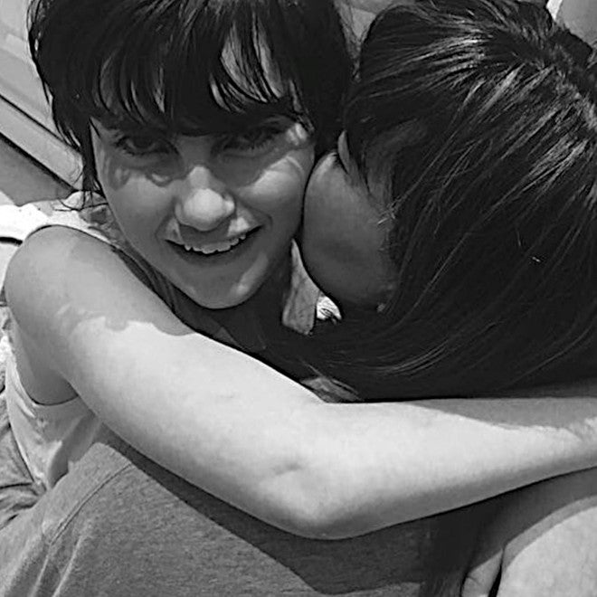 A black and white image of a smiling young woman being hugged by her mother