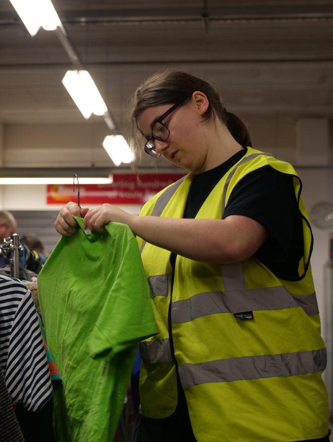A young woman in a high visibility jacket hanging clothes up in a charity shop