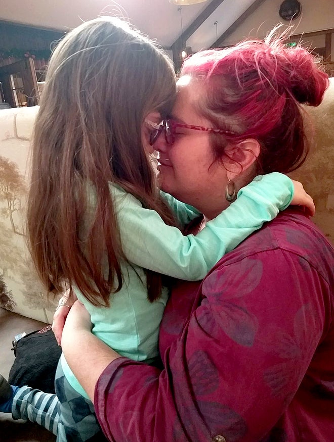A smiling woman hugging a young girl on the sofa at home