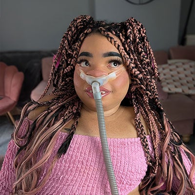 A photo of Shelby lynch. Her black and pink hair is braided and she wears a pink top. 